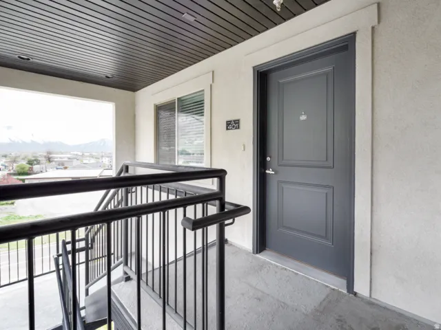 Exterior corridor with a dark panel door, textured exterior wall finish, and a black metal railing