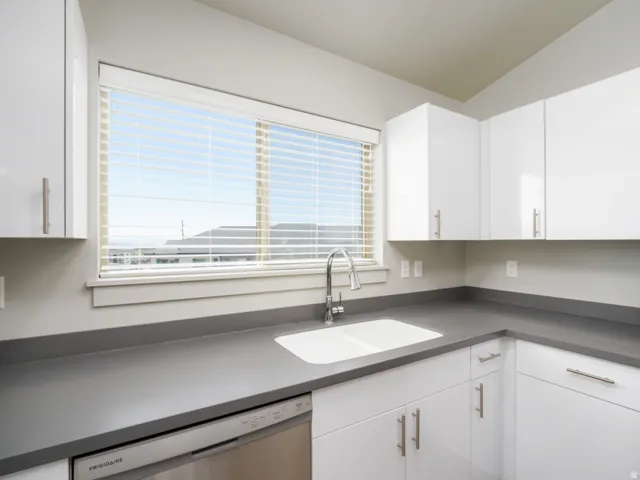 Contemporary kitchen featuring white cabinetry, a double basin sink with a gooseneck faucet, gray countertops, and a stainless steel dishwasher