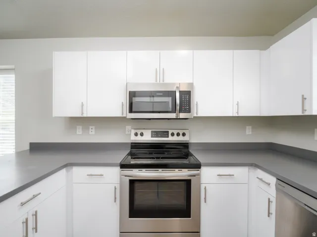 U-shaped kitchen featuring white cabinetry, gray countertops, stainless steel appliances, and a built-in microwave