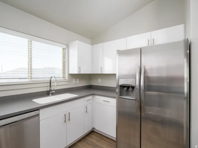 Stainless steel refrigerator, stainless steel dishwasher, white cabinetry, gray countertops, and wood-finish flooring