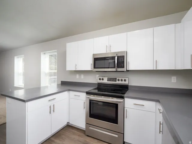 White cabinetry with stainless steel appliances, dark countertops, and wood-finish flooring