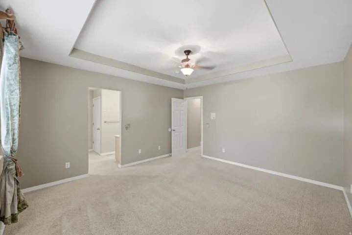 Tray ceiling with a ceiling fan, neutral carpeting, and light-toned wall paint