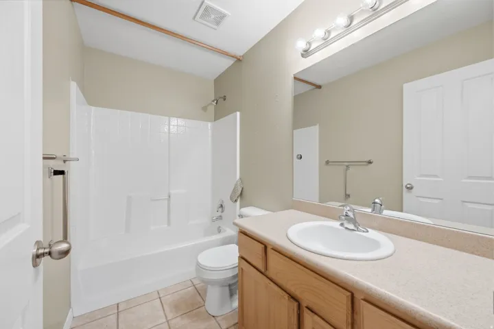 Bathroom featuring a neutral color palette, built-in bathtub with shower, vanity with an integrated sink, large mirror, and tiled flooring