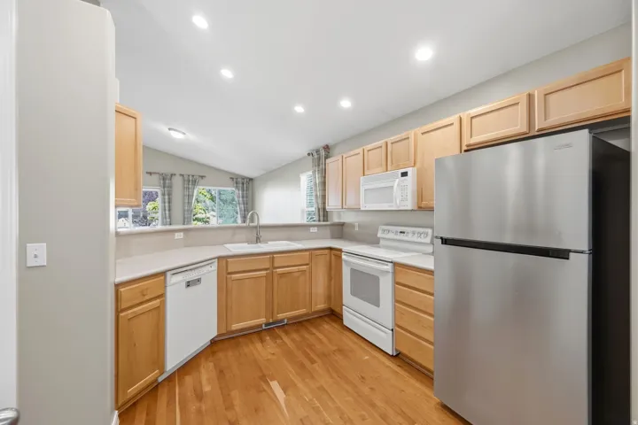 Corner kitchen featuring wood-finish flooring, light wood cabinetry, recessed lighting, and stainless steel appliances