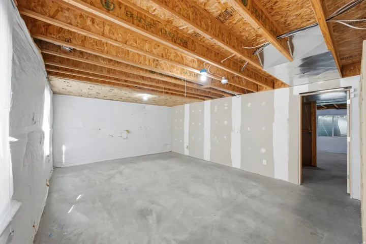Unfinished concrete flooring, exposed wood joists, partial drywall installation, insulated exterior wall, and unfinished interior framing