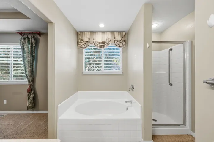 Built-in bathtub with tiled surround, adjacent to a glass-enclosed shower with white subway-style tile