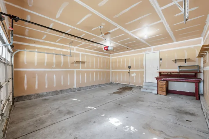 Concrete flooring garage with an automatic overhead door opener, exposed drywall, and built-in shelving
