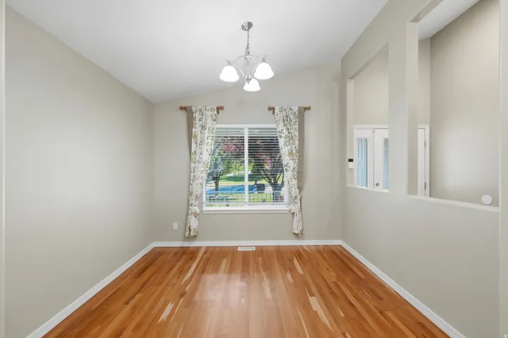 Hardwood flooring, vaulted ceiling, recessed wall accents, and an overhead chandelier fixture