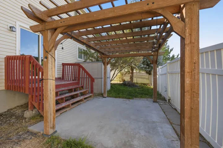 Paved patio with an attached wood pergola, complemented by a red-stained wood deck and a white privacy fence