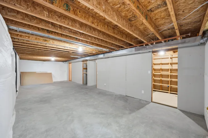 Unfinished lower level featuring exposed ceiling joists, concrete flooring, and built-in shelving