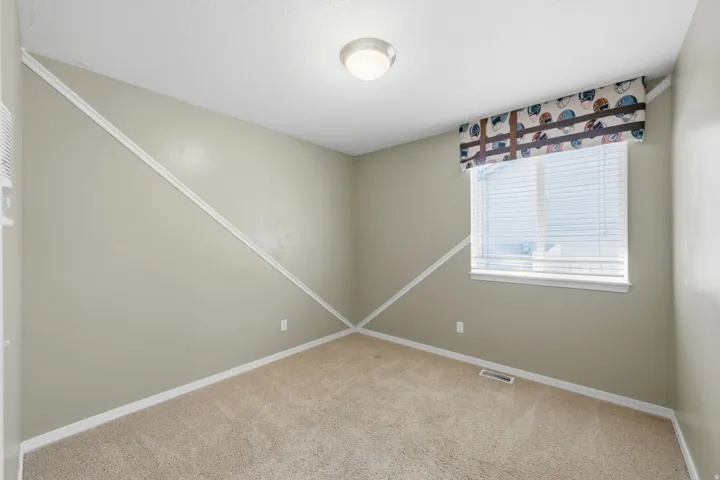 Neutral-toned wall paint, white trim accents, window with blinds, carpeted flooring, and flush-mount ceiling lighting