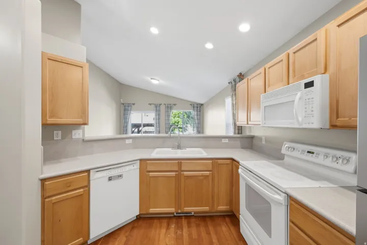 Kitchen featuring wood-finish cabinetry, light-toned countertops, and a white appliance suite including a dishwasher, range, and built-in microwave
