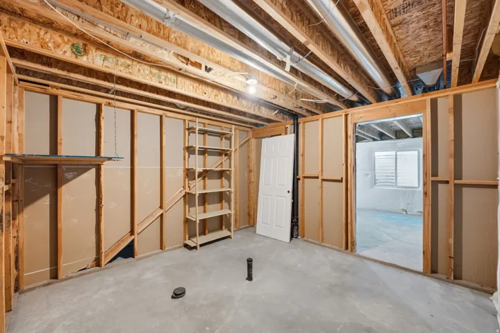 Unfinished basement space with exposed wood framing, concrete flooring, and built-in shelving