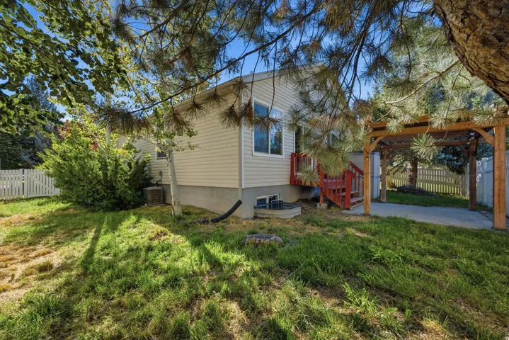 Wood pergola over concrete pad, white picket fencing, and wood deck with red-painted stairs