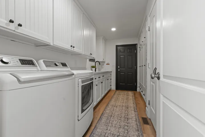 Laundry room featuring side-by-side washer and dryer, white cabinetry with hardware accents, stainless steel sink, wood-finish flooring. Pantry closet with ample space. Five storage lockers with shelves and hanging storage.