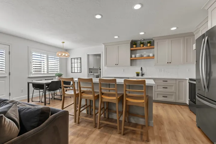 Open-concept kitchen featuring light-toned cabinetry, a spacious island with seating, wood-finish flooring, recessed lighting, and quartz countertops.