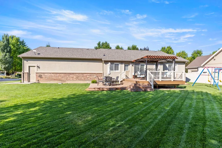 Expansive backyard featuring a manicured lawn, a multi-level wood-finish deck, a pergola, and a stucco exterior with brick accents
