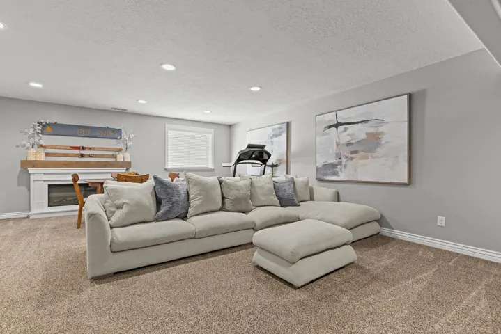 Spacious recreation room featuring a generous sectional sofa with ottoman, recessed ceiling lighting, and neutral carpet flooring