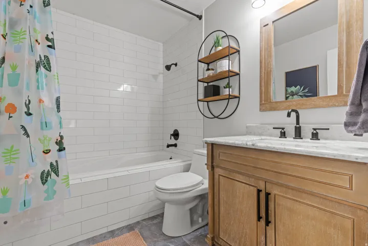 Spa-inspired bathroom featuring a wood-finish vanity with marble countertop, matte black hardware, large soaking tub, and an integrated sink