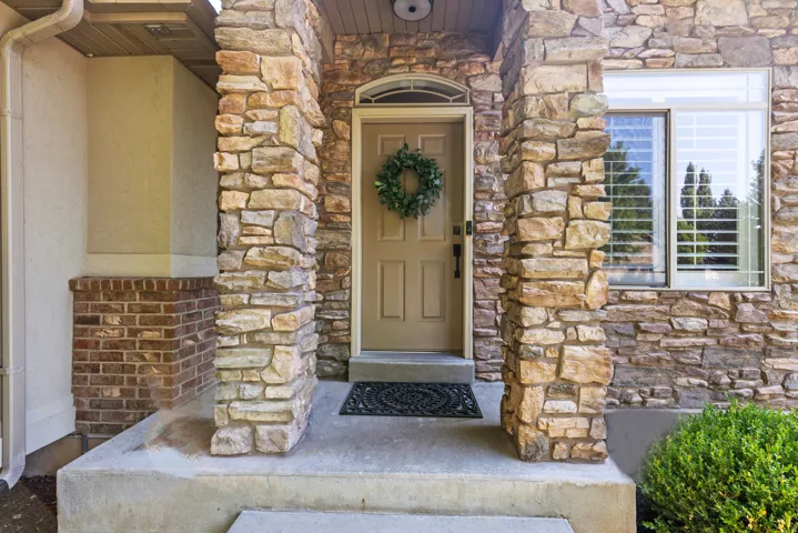 Stone facade entry featuring a welcoming front door with an arched transom, brick detailing, and a multi-paned window with plantation shutters