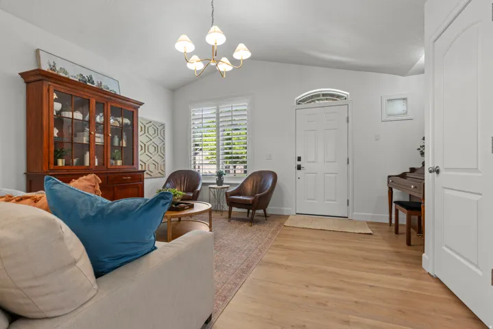 Vaulted ceiling living area featuring light wood-finish flooring, a white paneled entry door with an arched transom, and windows with white plantation shutters