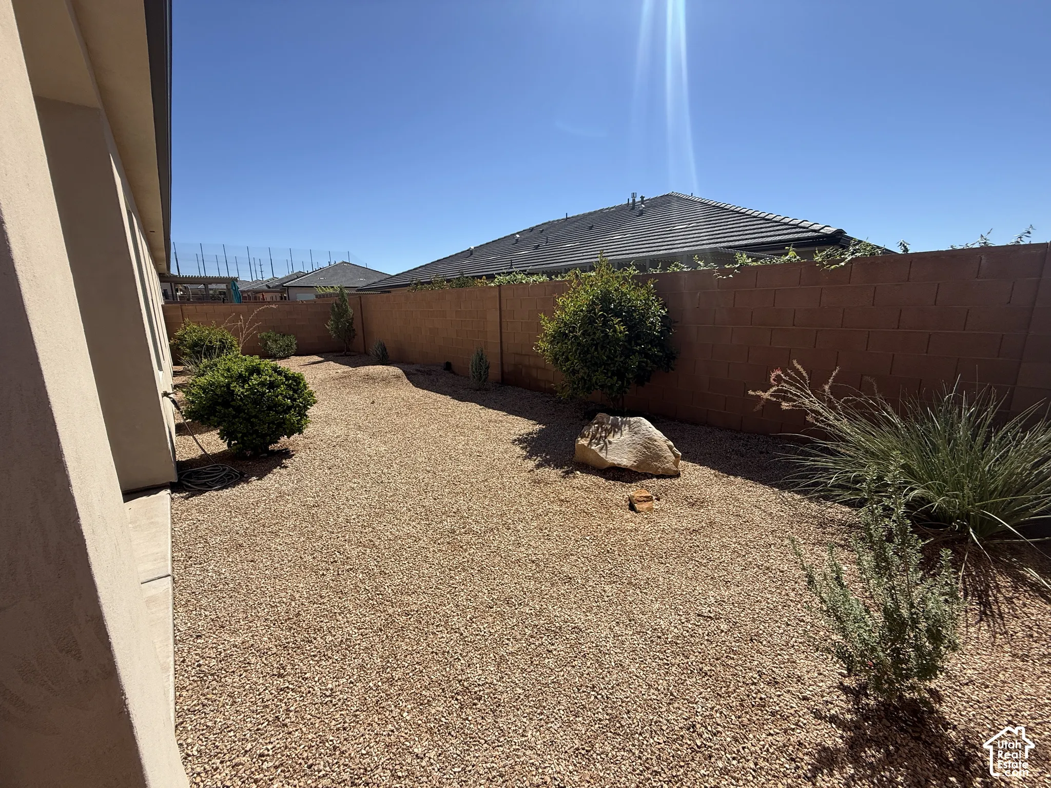Side yard featuring gravel landscaping, mature desert shrubs, a decorative landscape boulder, and a masonry perimeter wall