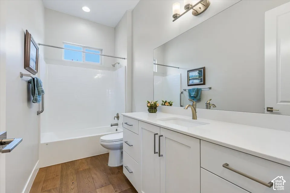 Bathroom featuring wood-finish flooring, a contemporary vanity with a white countertop, an undermount sink, and a built-in tub with white wall tiling