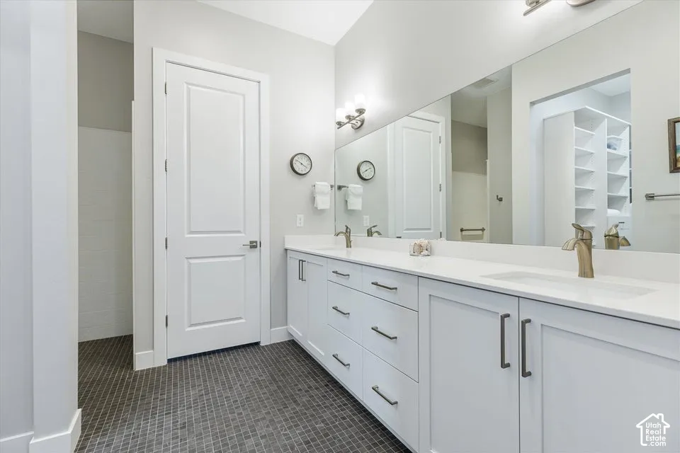 Dual vanity with white cabinetry and integrated sinks, a large wall-mounted mirror, and dark mosaic tile flooring