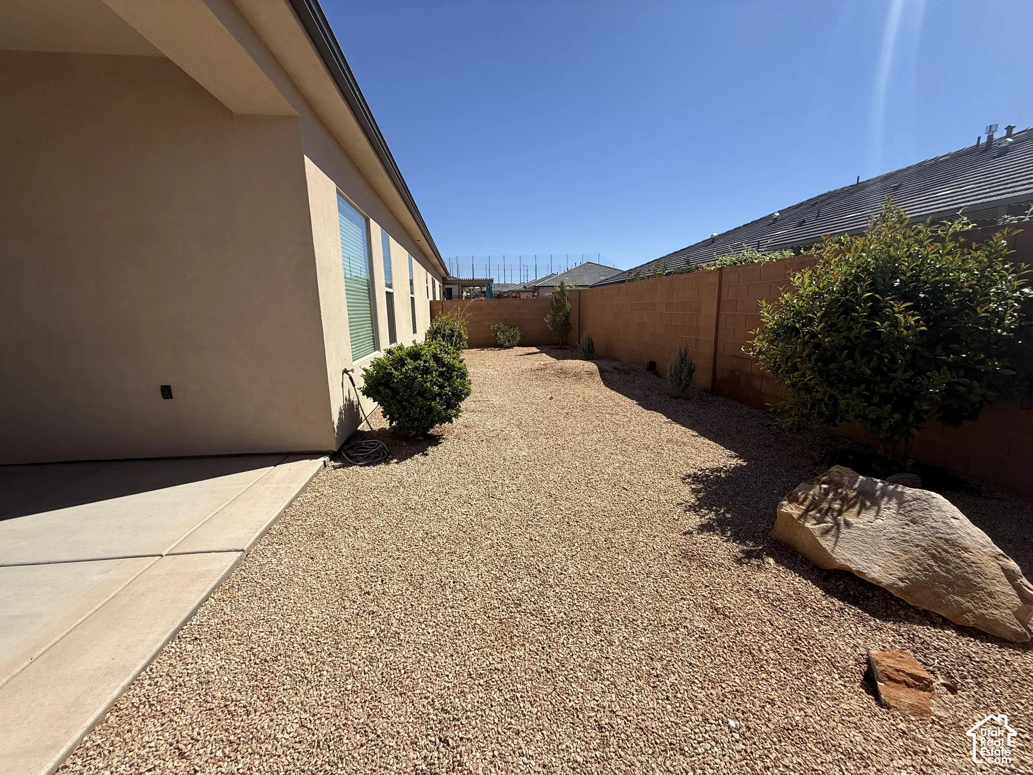 Side yard featuring a concrete patio, stone-covered ground, block wall perimeter, and decorative boulder