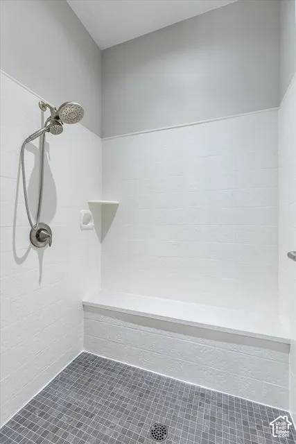 Modern shower enclosure featuring white subway tile walls, a brushed nickel showerhead with handheld spray attachment, gray mosaic tile flooring, and a recessed niche for toiletries