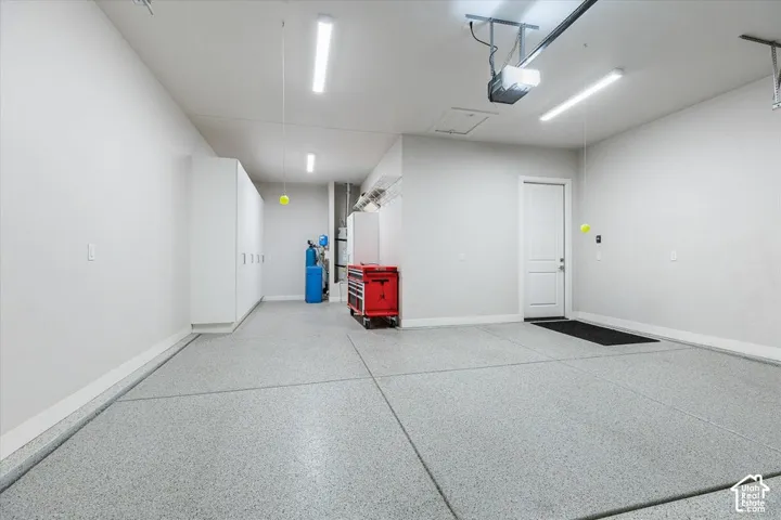 Epoxy-coated concrete flooring, white walls, built-in storage cabinetry, overhead lighting, and an automatic garage door opener