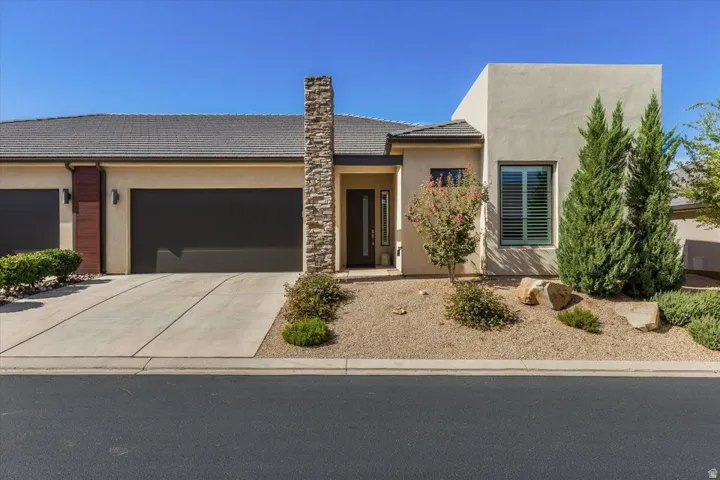 Contemporary stucco exterior with a tiled roof, stone pillar accent, and a single-panel garage door