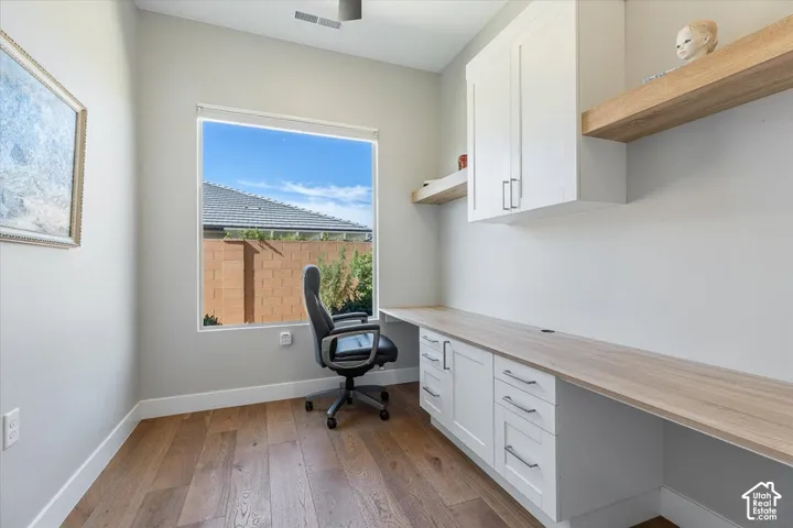 Built-in desk with wood-finish countertop, shaker-style cabinetry with silver-tone hardware, and wood-finish flooring