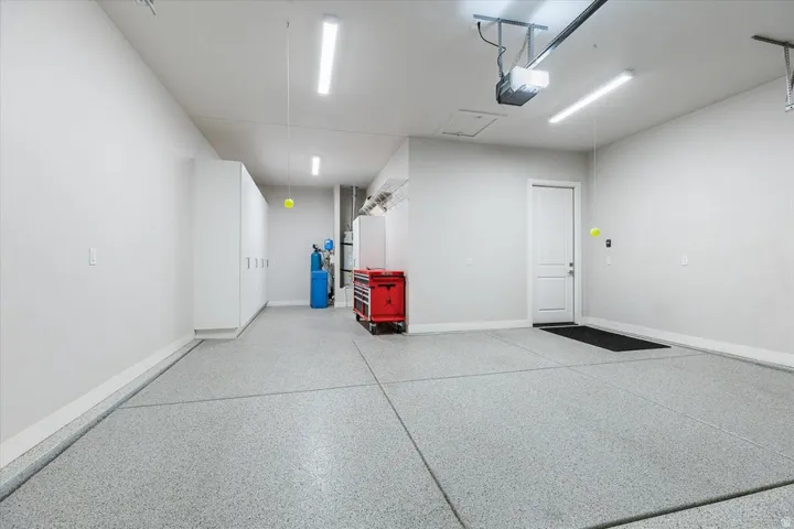 Epoxy-coated concrete flooring, white walls, built-in storage cabinetry, overhead lighting, and an automatic garage door opener