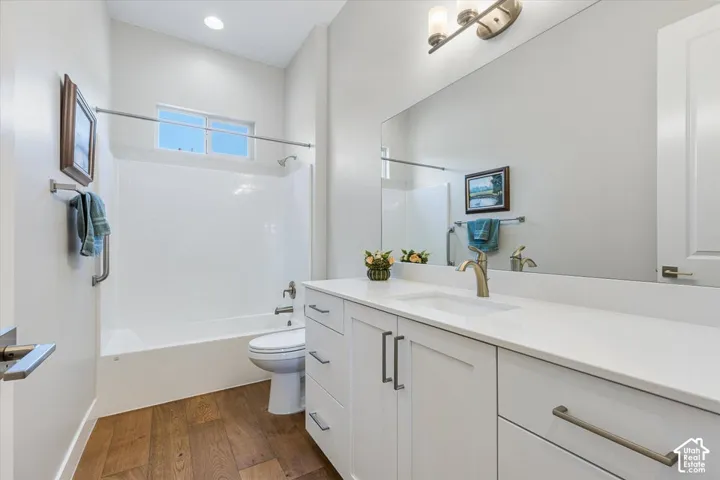 Bathroom featuring wood-finish flooring, a contemporary vanity with a white countertop, an undermount sink, and a built-in tub with white wall tiling