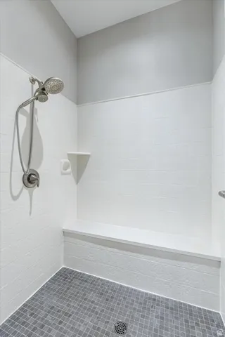 Modern shower enclosure featuring white subway tile walls, a brushed nickel showerhead with handheld spray attachment, gray mosaic tile flooring, and a recessed niche for toiletries