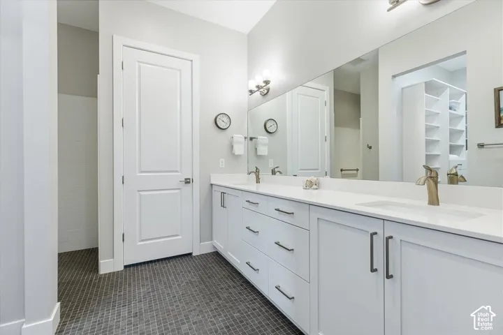 Dual vanity with white cabinetry and integrated sinks, a large wall-mounted mirror, and dark mosaic tile flooring