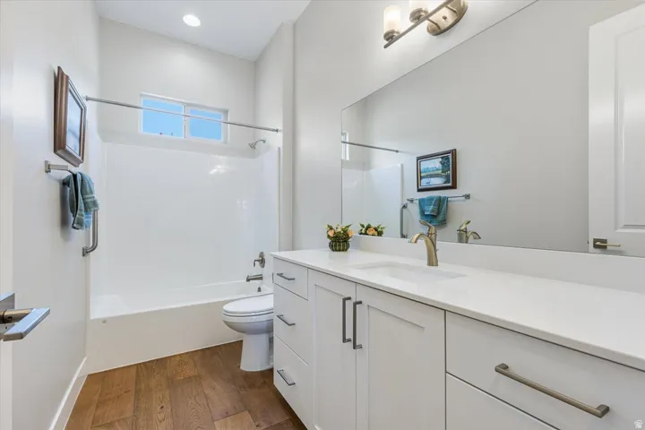 Bathroom featuring wood-finish flooring, a contemporary vanity with a white countertop, an undermount sink, and a built-in tub with white wall tiling