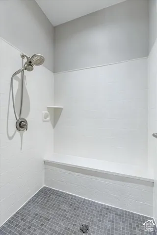 Modern shower enclosure featuring white subway tile walls, a brushed nickel showerhead with handheld spray attachment, gray mosaic tile flooring, and a recessed niche for toiletries
