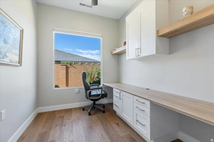 Built-in desk with wood-finish countertop, shaker-style cabinetry with silver-tone hardware, and wood-finish flooring