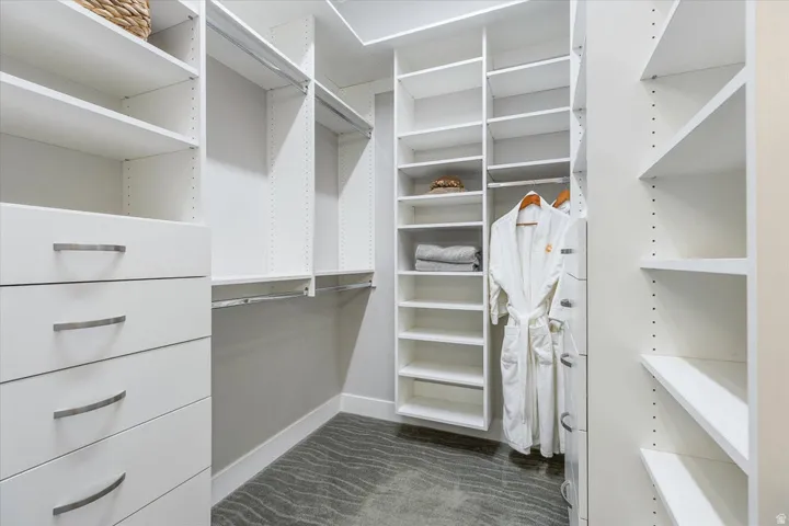 Walk-in closet featuring built-in white shelving, integrated drawers with curved handles, multiple hanging rods, and patterned carpeting