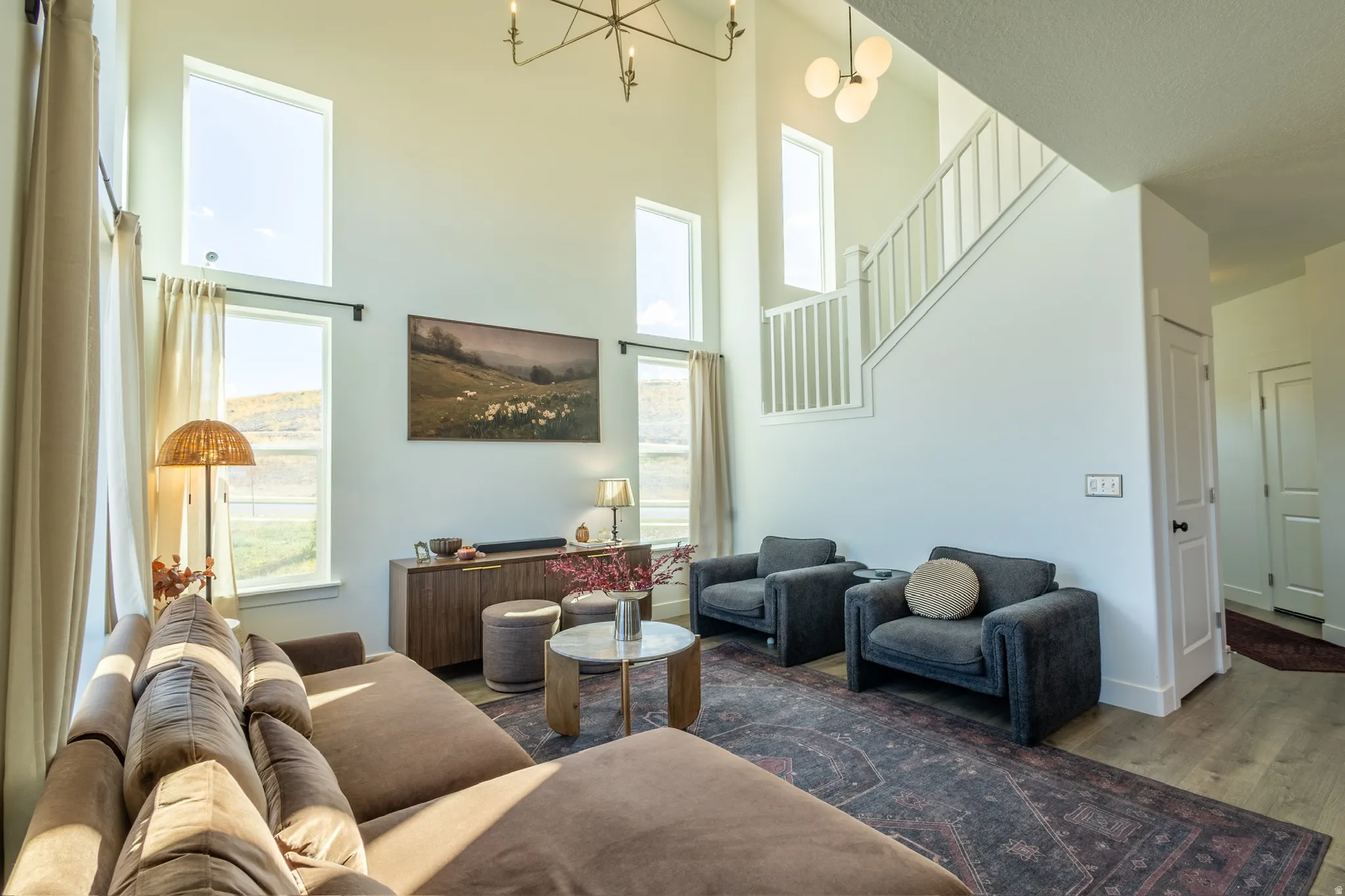 Two-story living area featuring tall windows, wood-finish flooring, a contemporary chandelier, and a white staircase with balusters