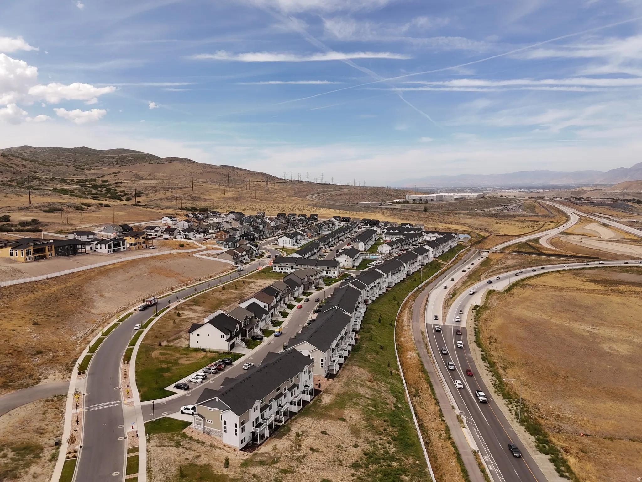 Expansive residential development with multiple building types, mountain backdrop, paved roadways, and highway access