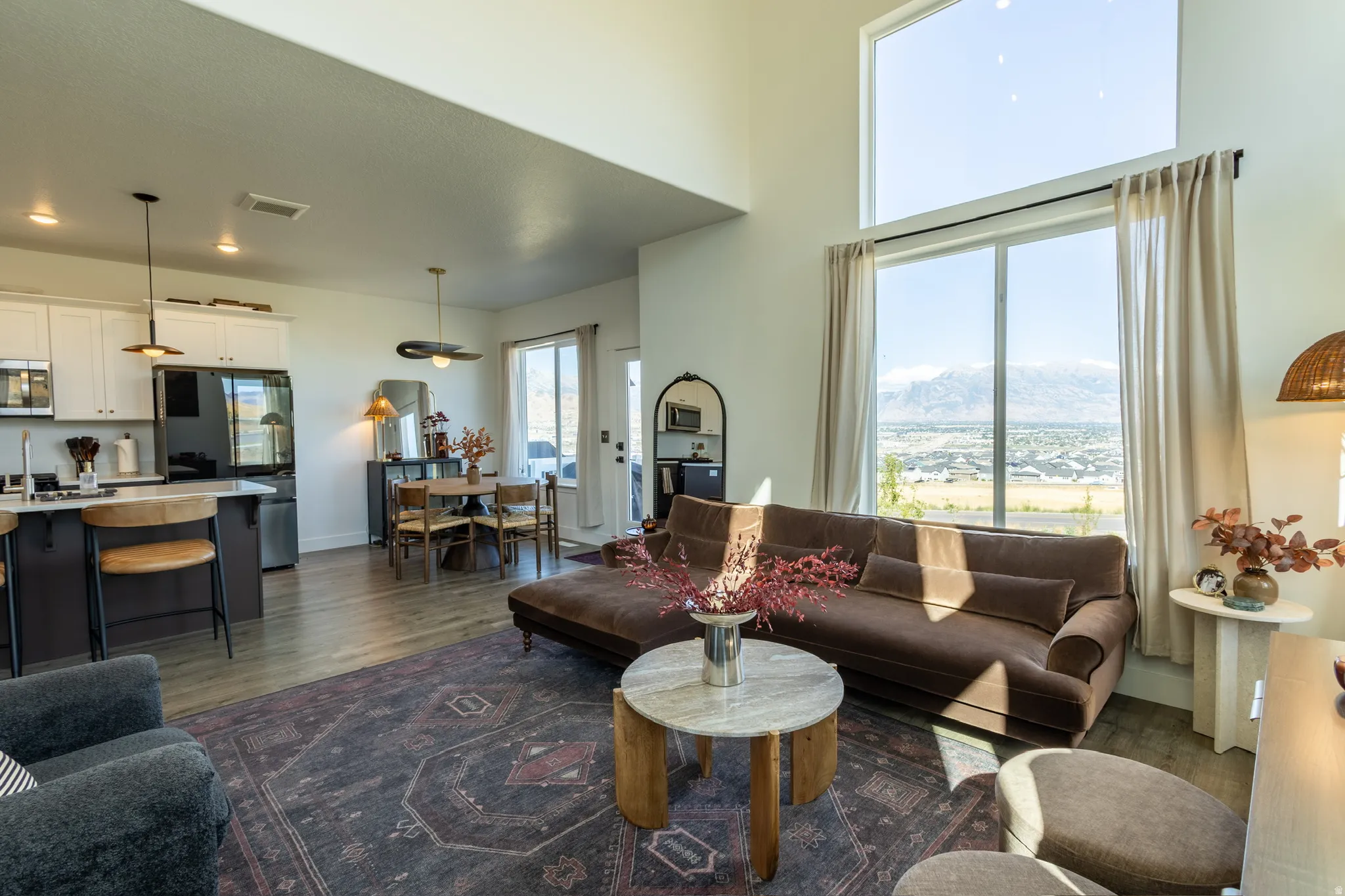 Voluminous ceiling height, expansive windows, mountain scenery, light wood-finish flooring, and a modern kitchen with white cabinetry