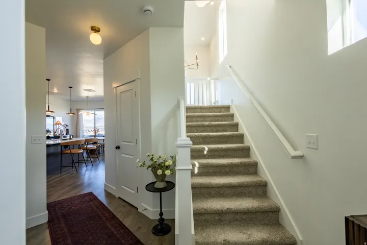Carpeted staircase with white railing, wood-finish flooring, and bright white walls