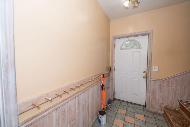 Entryway featuring wood-finish wainscoting, a coat rack with wooden pegs, a paneled door with an arched window, and patterned tile flooring