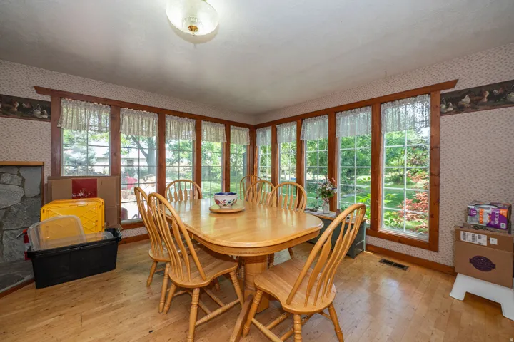 Expansive window array, hardwood flooring, stone fireplace, and ceiling-mounted light fixture
