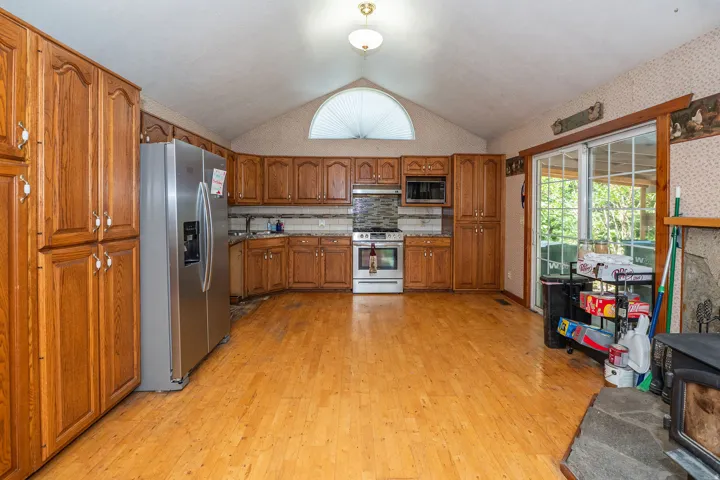 Vaulted ceiling with an arched window, wood-finish flooring, wood cabinetry, stainless steel appliances, and sliding glass doors