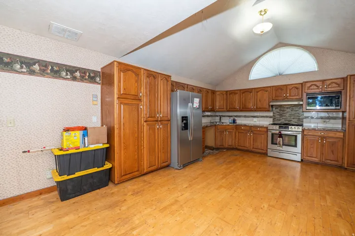 Wood-finish flooring, vaulted ceiling, stainless steel appliances, wood cabinetry, and a half-round window