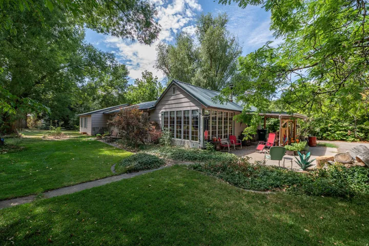 Siding exterior with a metal roof, full-light sunroom, covered patio, and established landscaping